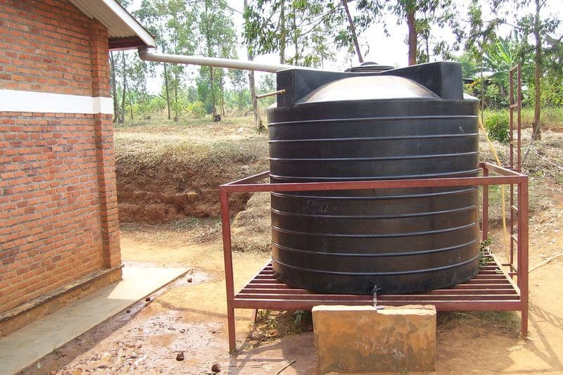 Cuve de récupération d'eau de pluie reliée à la gouttière d'un bâtiment en briques (Rwanda)