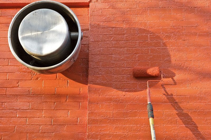 Rouleau appliquant une peinture orange sur un mur de briques