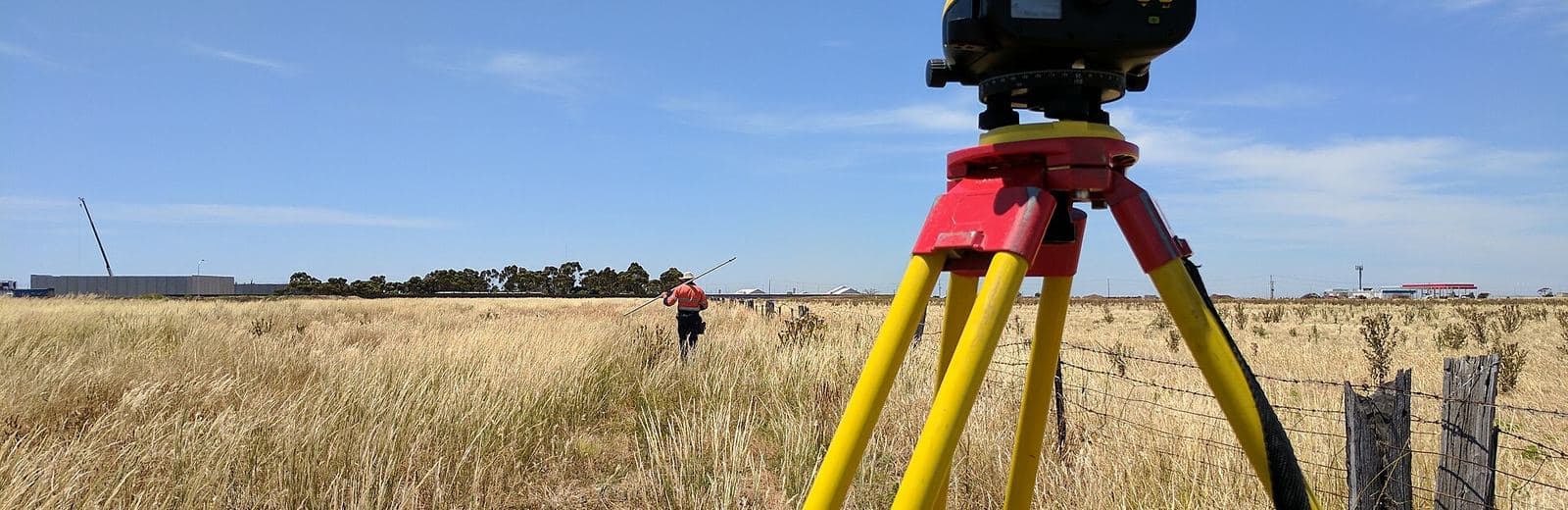 Niveau optique sur trépied et technicien de terrain dans un champ